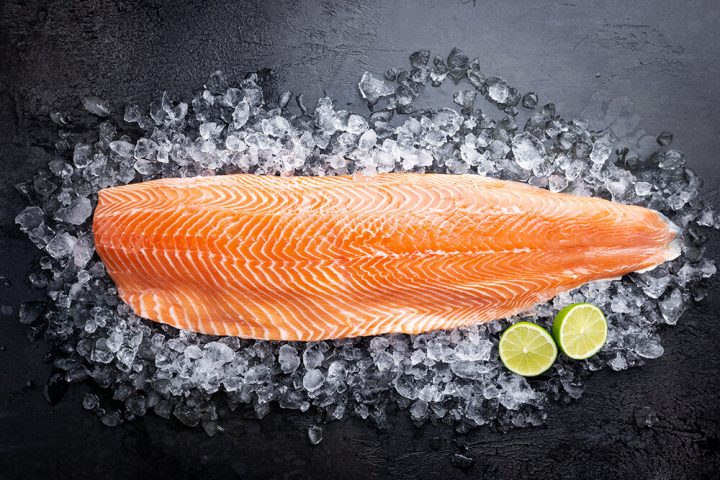 Fresh raw salmon or trout sea fish fillet on ice on black background, top view